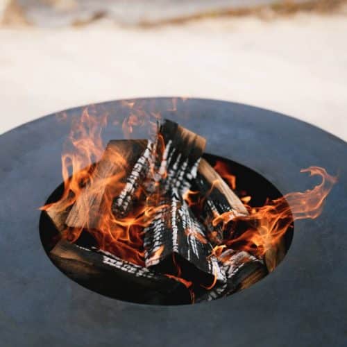 home improvement contractors close-up of a wood fire inside a metal firepit bowl outdoors.