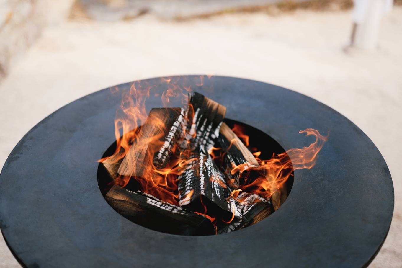 close-up of a wood fire inside a metal firepit bowl outdoors.