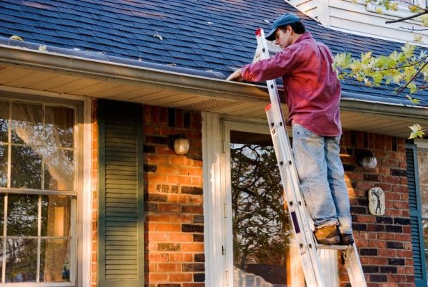 A homeowner on a ladder cleaning his gutters, removing debris, build-up, and checking for issues.