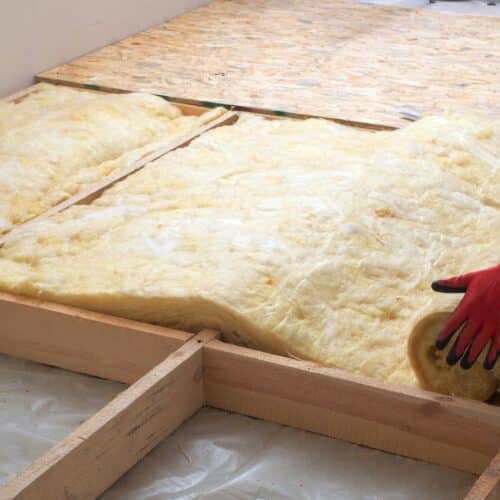 home improvement contractors A person wearing red and black gloves and a black jumpsuit is applying insulation to a home's floor.