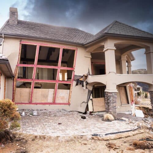 home improvement contractors A home with a crumbling foundation that’s suffered significant fire damage. There’s smoke in the sky behind it.