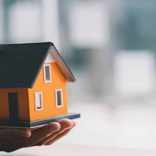 home improvement contractors A miniaturized home in the palm of someone's hand is next to three stacks of quarters in varying heights.