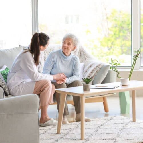 home improvement contractors A senior loved one sitting with a family member having a conversation on a gray sofa. There's a coffee table in front.