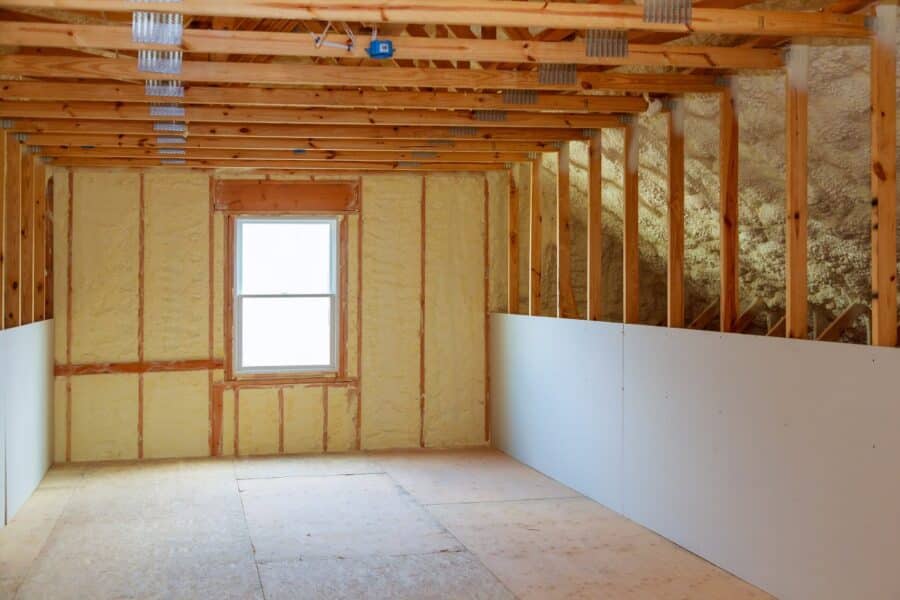 A home under construction with the studs and rafters bare. There’s spray foam insulation between them.