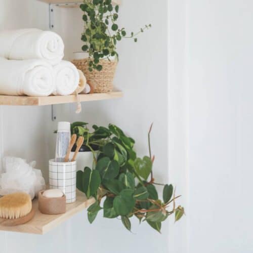 home improvement contractors Wooden floating shelves in the bathroom holding neatly arranged body care tools, folded towels, and plants.