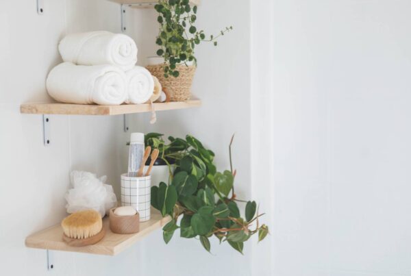 Wooden floating shelves in the bathroom holding neatly arranged body care tools, folded towels, and plants.