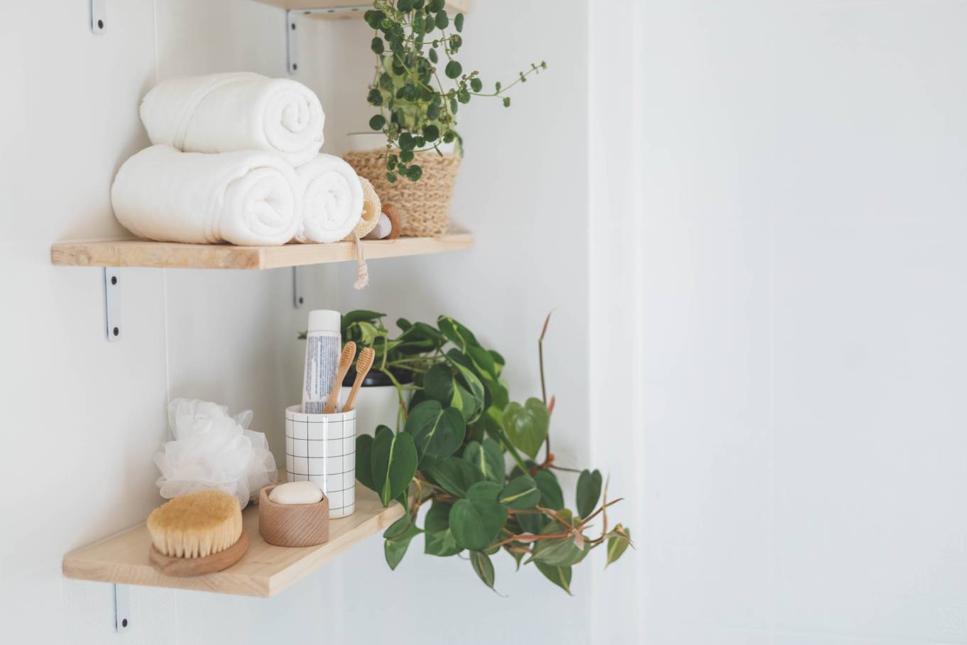 Wooden floating shelves in the bathroom holding neatly arranged body care tools, folded towels, and plants.