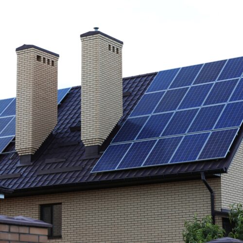 home improvement contractors A side view of a home made of beige bricks with two chimneys and solar panels installed on the roof.