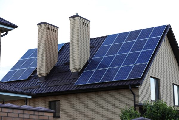 A side view of a home made of beige bricks with two chimneys and solar panels installed on the roof.