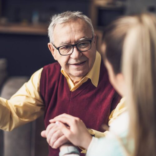 helloproject An older man wearing glasses and holding onto a cane in his left hand looks ahead at a woman who holds his hand.