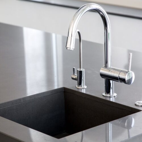 home improvement contractors A pristine washing station in a gray kitchen island with a tall chrome faucet and a deep, square sink.