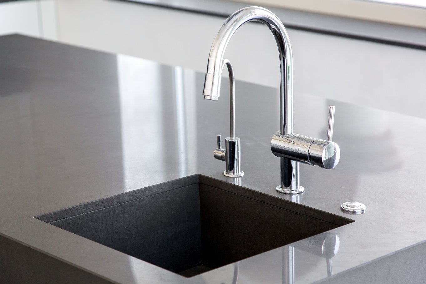 A pristine washing station in a gray kitchen island with a tall chrome faucet and a deep, square sink.