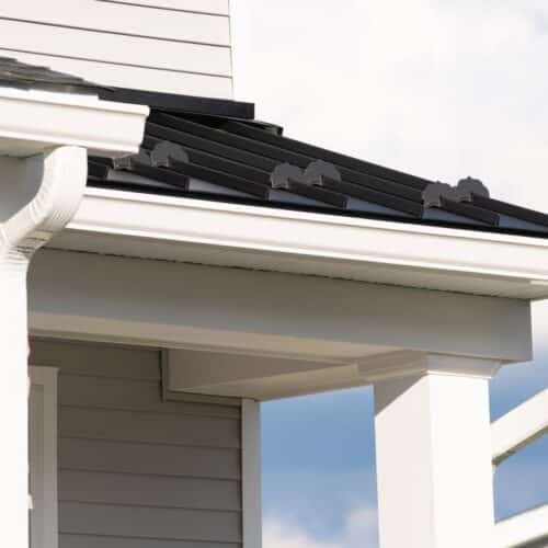 home improvement contractors The corner of a home's roof has white gutters, a white downspout, black metal roofing, and gray shingles.
