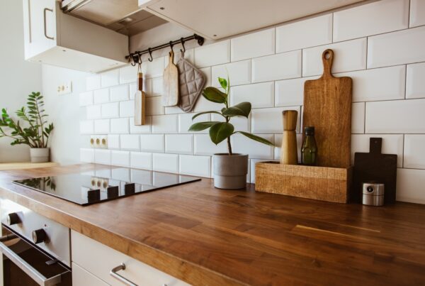 A wooden kitchen countertop with a stovetop on the left. A potted plant, a chopping board, and spices sit on the counter.
