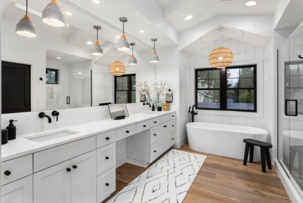 A beautiful, very white bathroom with a large window above the tub and a luxury vanity with a wall-length mirror.