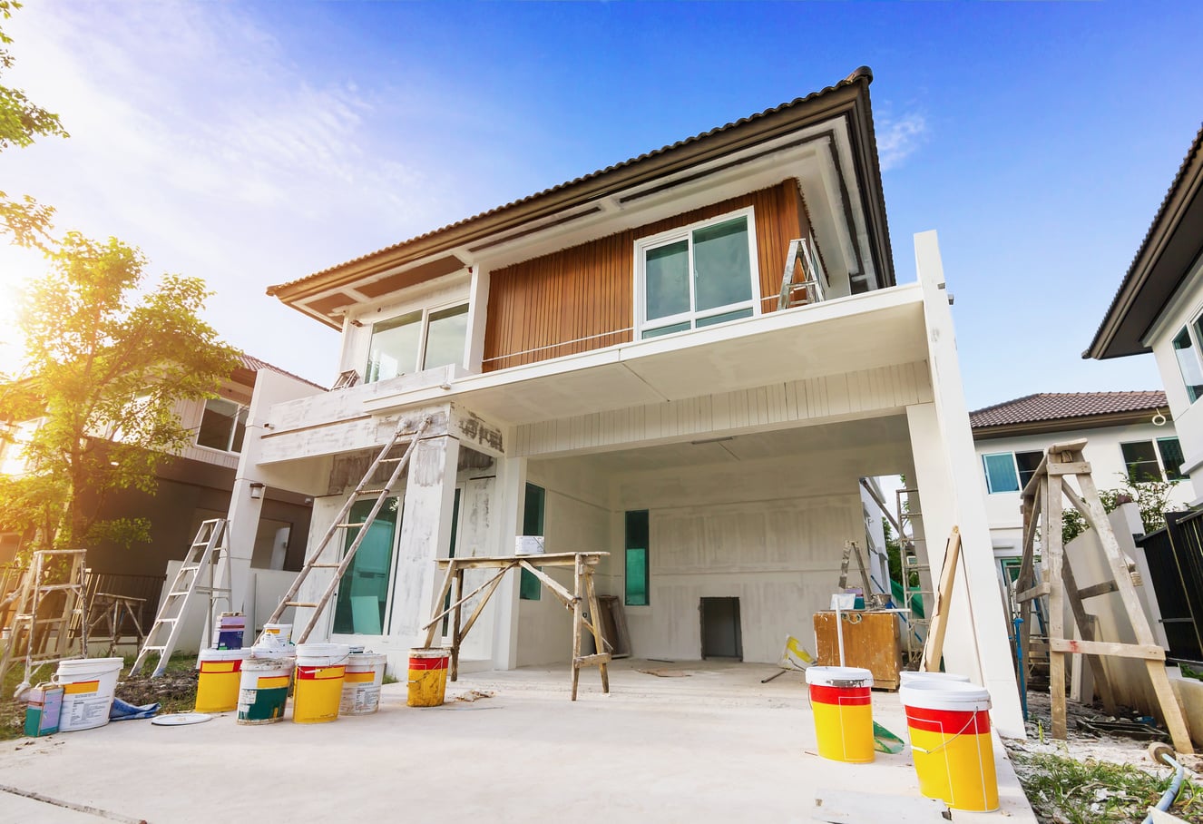 Two-story home with a large open garage undergoing renovation with multiple ladders and buckets on the outside.