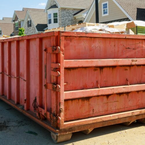 home improvement contractors A red roll-off dumpster filled with construction debris sits in front of a house undergoing renovations.