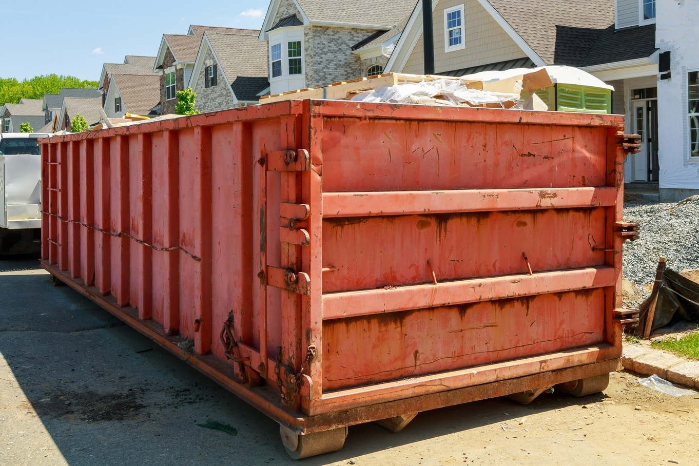 A red roll-off dumpster filled with construction debris sits in front of a house undergoing renovations.