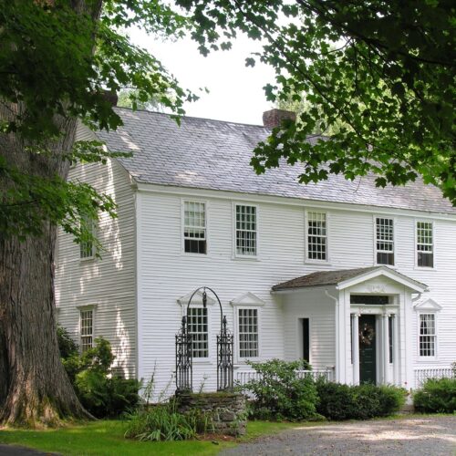 home improvement contractors A white vintage home's exterior. Greenery surrounds the house with a large tree and stone well to the left.