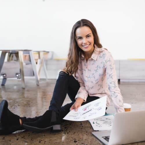 helloproject A woman is sitting on a polished concrete floor with a laptop and some papers. The floor is brown with distinct speckles.