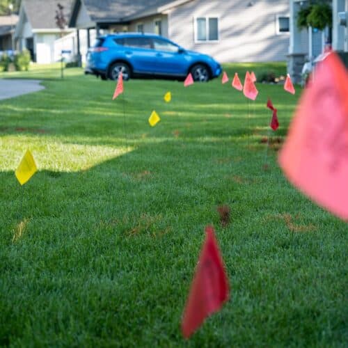 home improvement contractors The front lawn of a home in a cul-de-sac with red utility flags blurred in the foreground and more in the background.