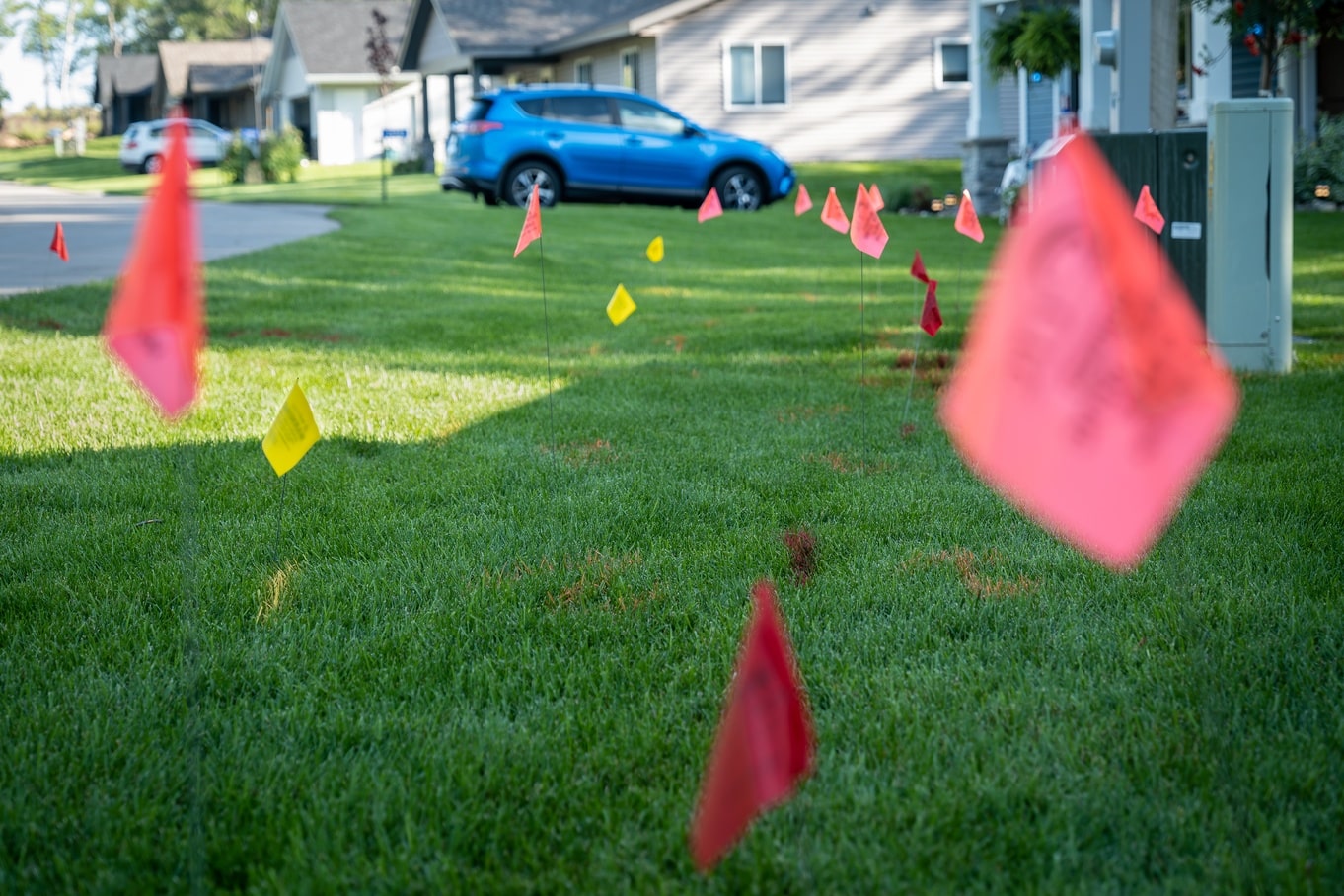 The front lawn of a home in a cul-de-sac with red utility flags blurred in the foreground and more in the background.