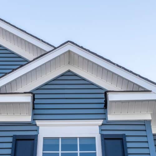home improvement contractors A home with a gable roof, white soffit, and blue siding against a pale blue sky.