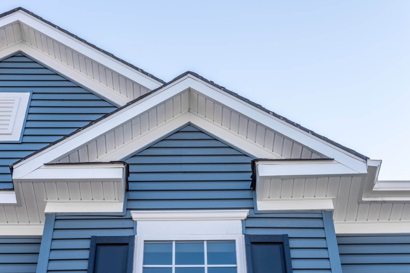 A home with a gable roof, white soffit, and blue siding against a pale blue sky.