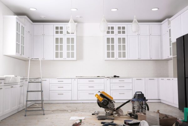 A kitchen that has several tools on the floor. There is a step ladder to the left side and cabinets along the wall.