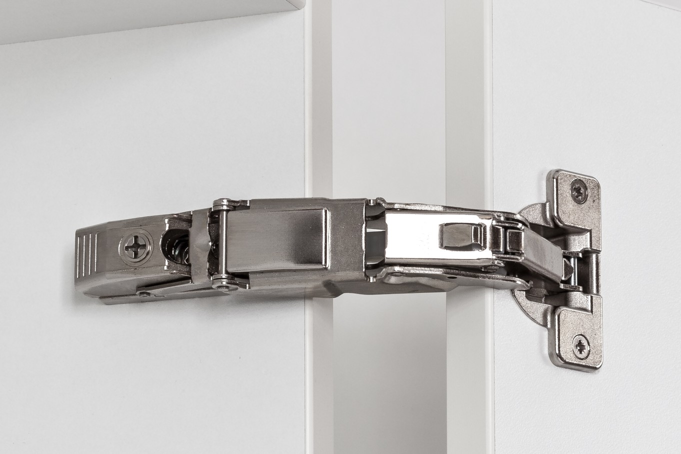 Close-up of a soft-close hinge on the inside of a cabinet and a cabinet door. The white cabinet door is open wide.