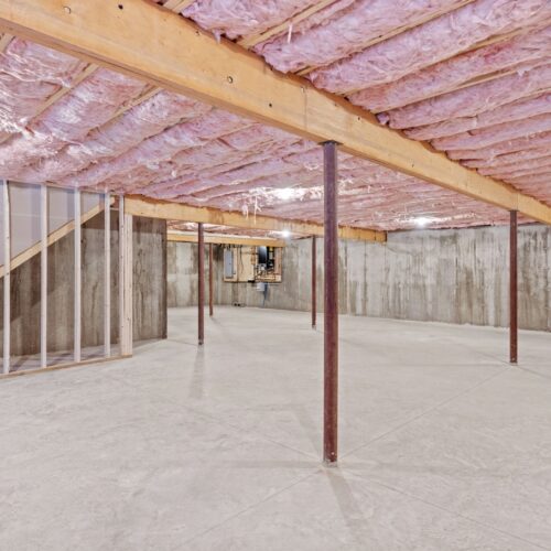 helloproject A wide view of an unfinished basement in a home with concrete floors and pink insulation in the ceiling.