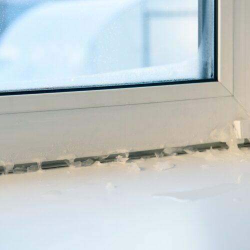 home improvement contractors Close-up of a frosted window frame and sill with visible ice buildup, highlighting insulation issues in cold weather.
