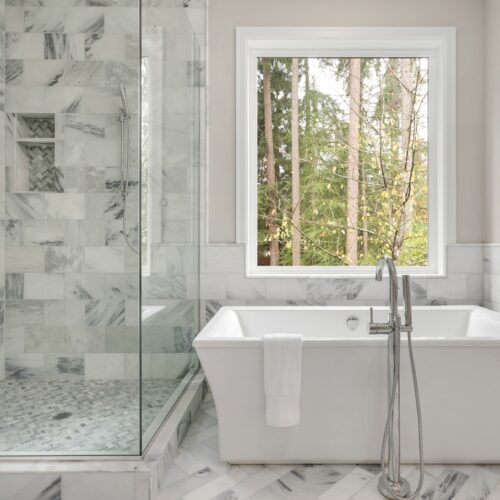 home improvement contractors A modern bathroom complete with a standalone tub, a glass-enclosed shower, and a window offering views of a forest.