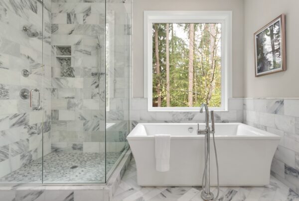 A modern bathroom complete with a standalone tub, a glass-enclosed shower, and a window offering views of a forest.