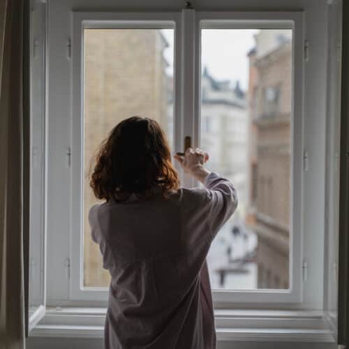 home improvement contractors A person standing in front of a two-pane window and reaching up to twist the window's latch-style lock.