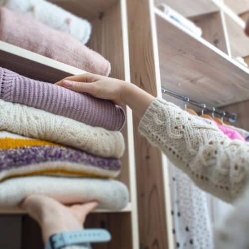 home improvement contractors A woman placing a pile of folded up clothes into a cubby in her closet. Clothes are also hanging behind her.