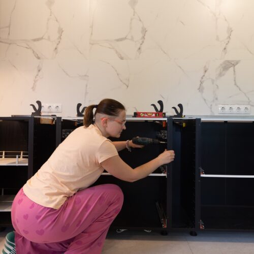 home improvement contractors A woman is kneeling down next to some kitchen cabinets. She’s using a drill to install new hardware.