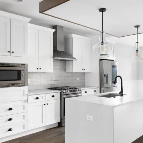 home improvement contractors A renovated kitchen features white cabinets, a kitchen island with waterfall countertops, and stainless steel appliances.