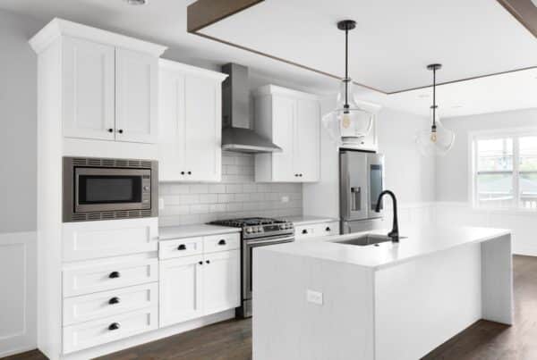 A renovated kitchen features white cabinets, a kitchen island with waterfall countertops, and stainless steel appliances.