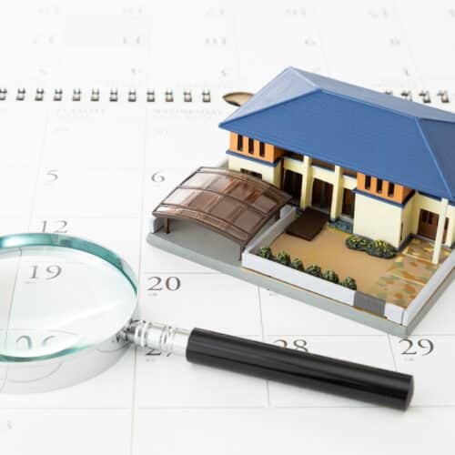 home improvement contractors A close-up of a model home with a blue roof placed next to a magnifying glass on top of a white calendar lying flat.