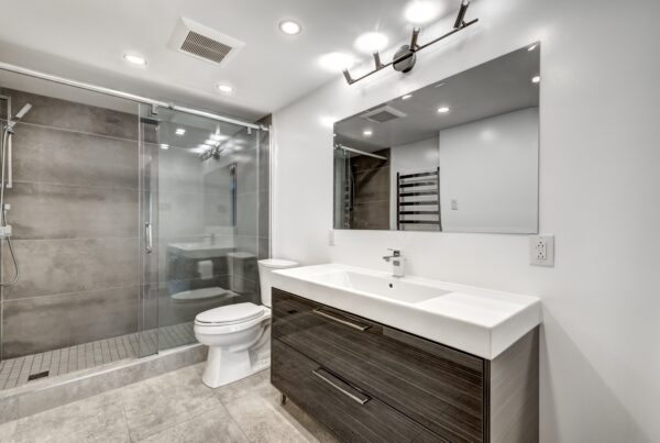 An updated and modern bathroom features a walk-in shower with a sliding glass door, a toilet, and a large single-sink vanity.