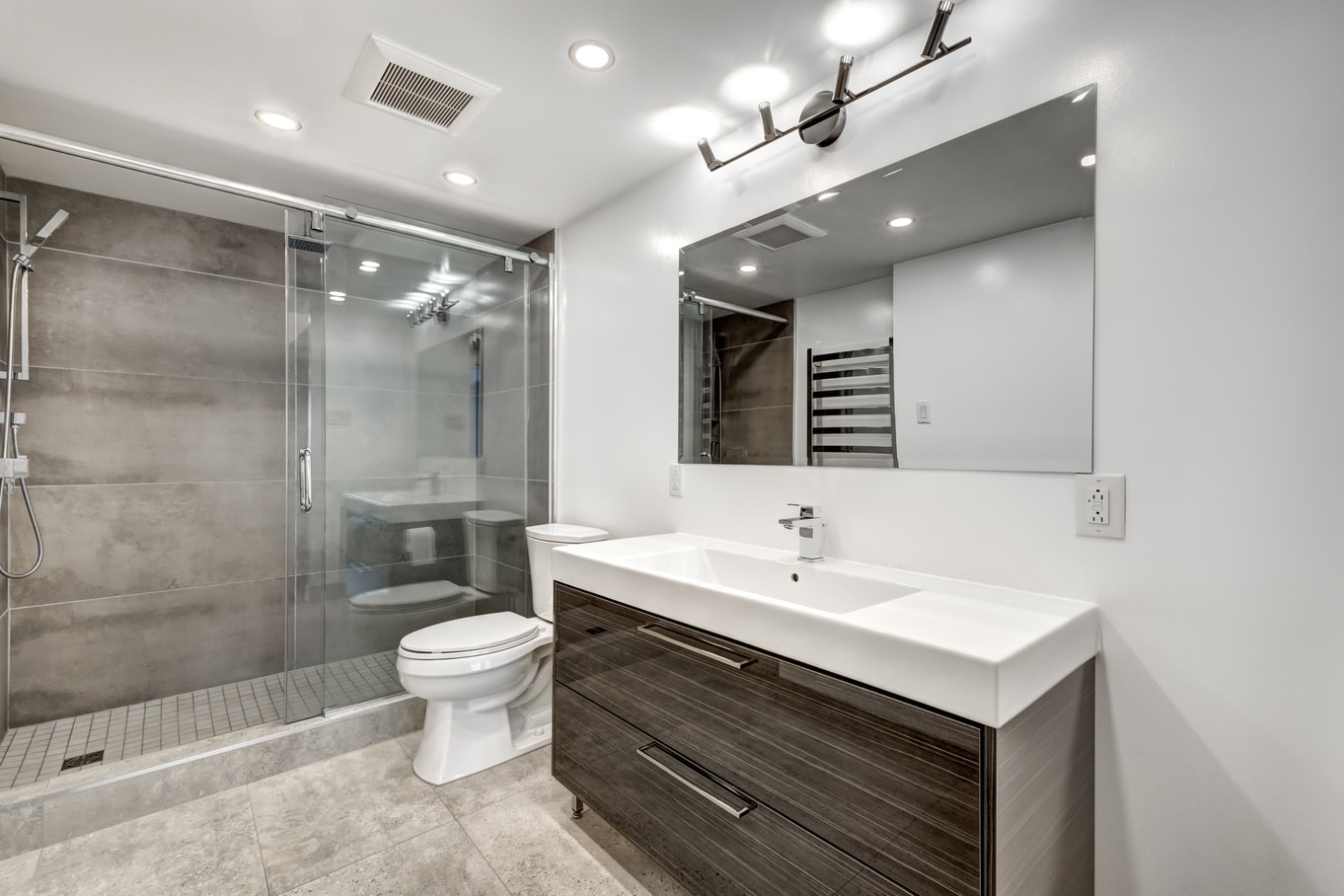 An updated and modern bathroom features a walk-in shower with a sliding glass door, a toilet, and a large single-sink vanity.