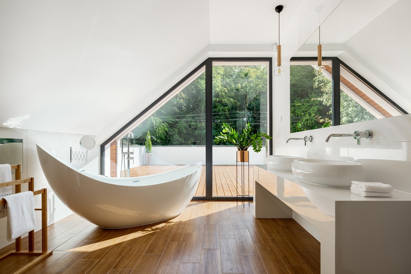 An attic bathroom with a freestanding bathtub, wood floor, sloped ceiling, and large glass doors to a balcony.