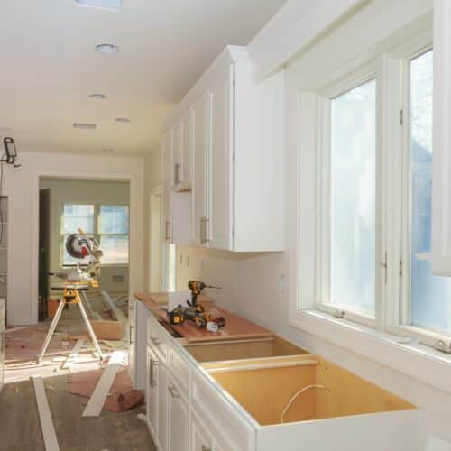 home improvement contractors The interior of a home's kitchen during a remodel with white, unfinished kitchen cabinets, a tabletop saw, and more.