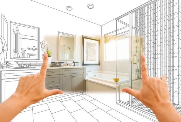 Hands frame a bathroom remodel rendering with a vanity, a tub, and a glass shower in a bright design sketch.