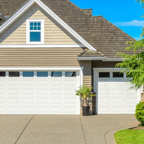 home improvement contractors A two-story home with a three-car garage. The garage doors are white with rectangular windows on the top row of panels.