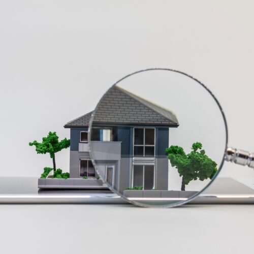 home improvement contractors A point of view looking through a magnifying glass at a miniature-scale model of a grey home with trees.