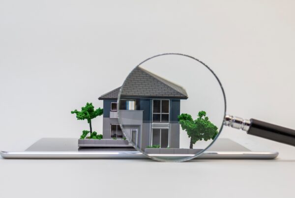 A point of view looking through a magnifying glass at a miniature-scale model of a grey home with trees.