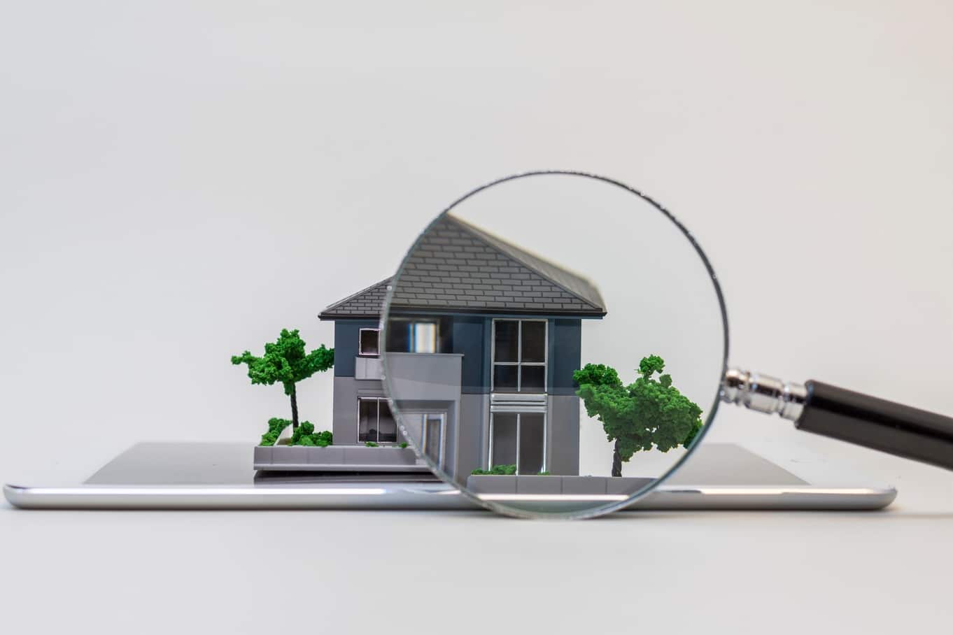 A point of view looking through a magnifying glass at a miniature-scale model of a grey home with trees.