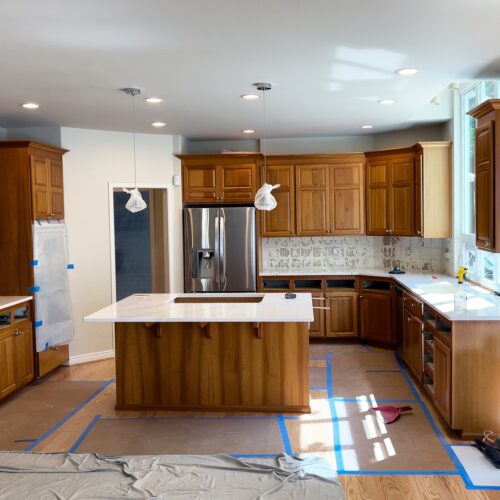 home improvement contractors A home kitchen under renovation with quartz countertops, dark wood cabinetry, and coverings to protect materials.